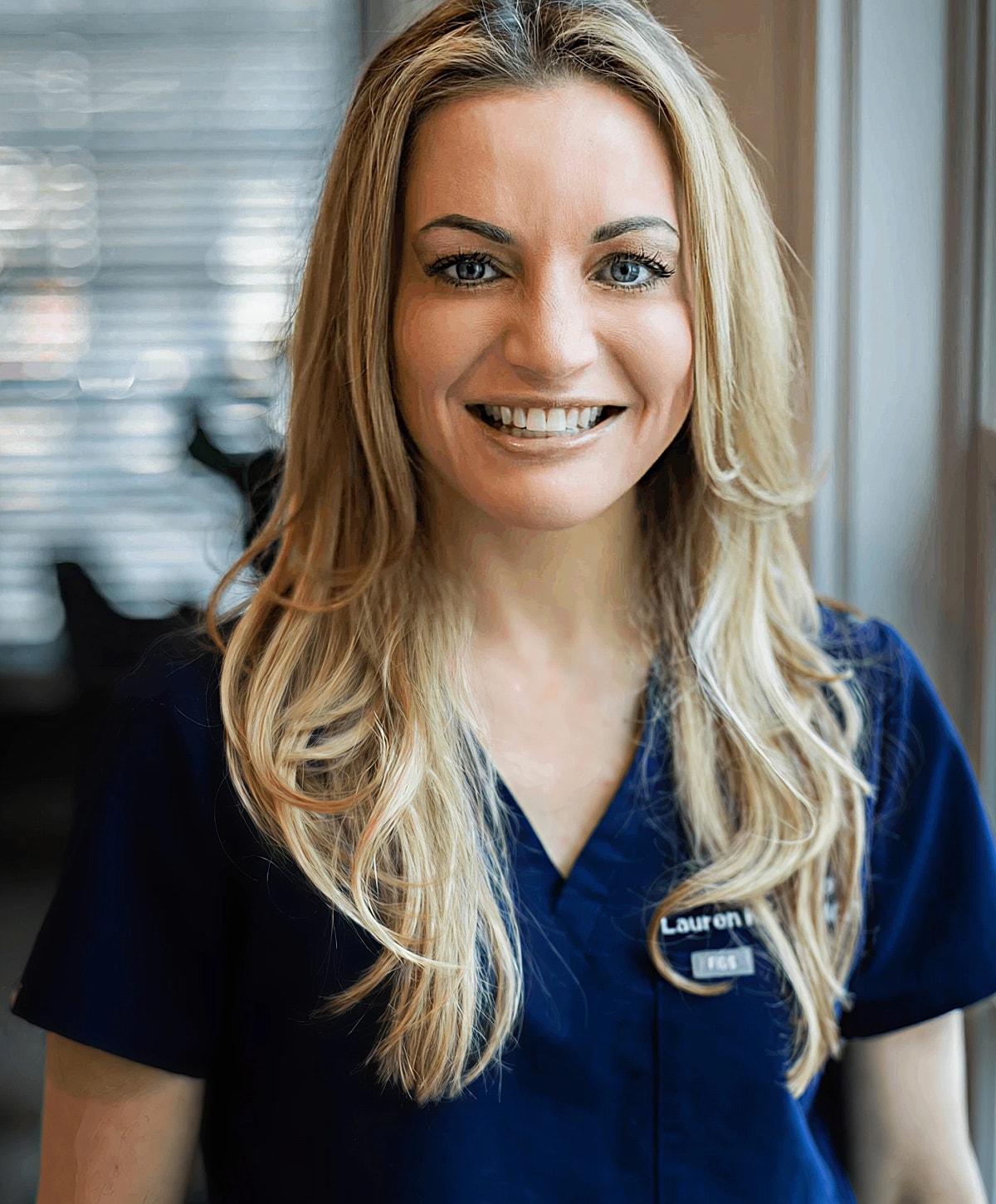 Smiling woman in medical scrubs, professional setting.