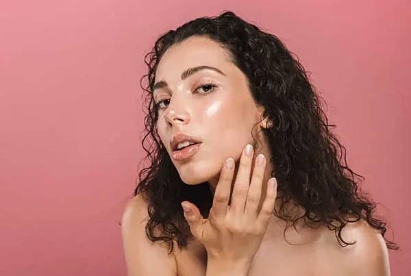 Woman touching her face against pink background.